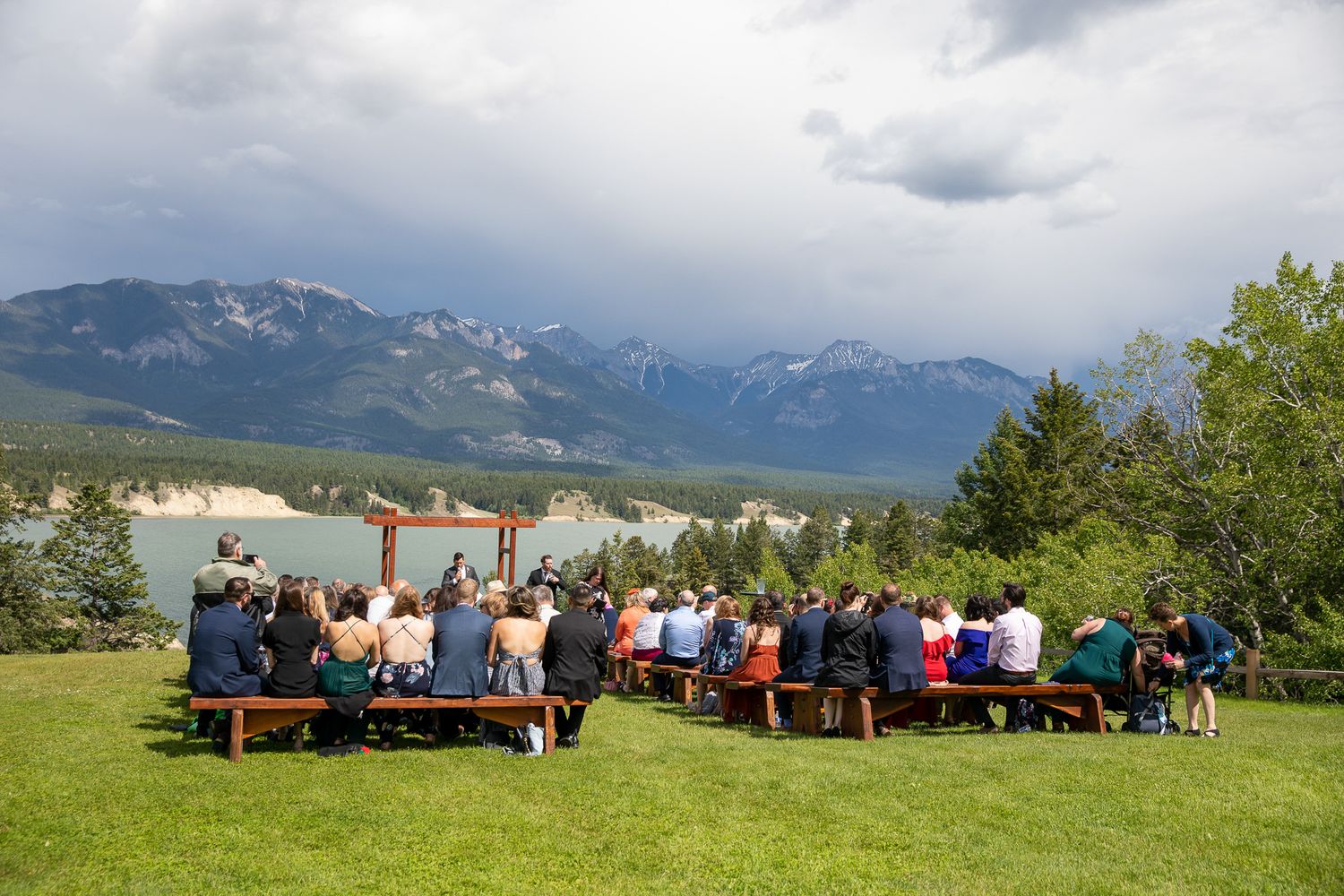 Panoramic view of outdoor seating with people enjoying mountain scenery on a cloudy day. Brady Creek ranch. Invermere, BC.