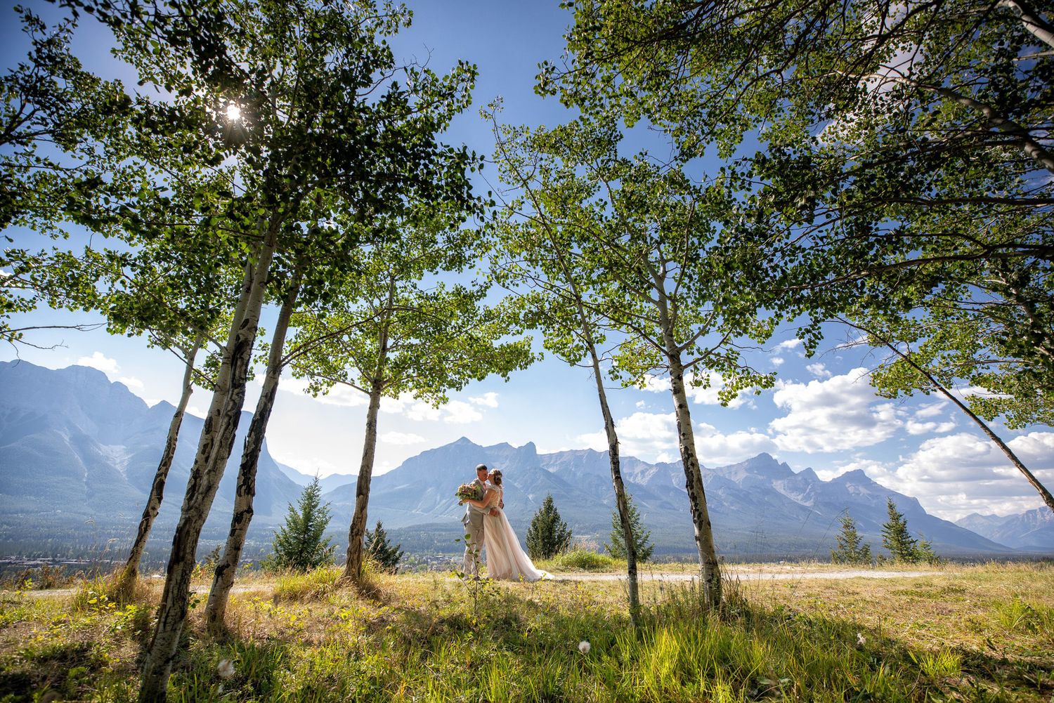 A panoramic view of snow-capped mountains and trees against a blue sky with white clouds in Invermere, British Columbia.