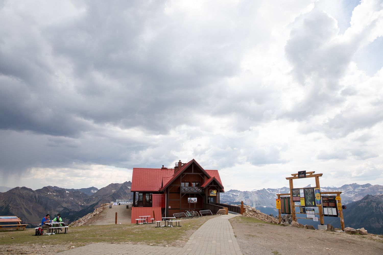 A rustic red-roofed mountain lodge sits atop a scenic alpine summit under dramatic cloudy skies at Kicking Horse Resort, Eagle Eye venue BC
