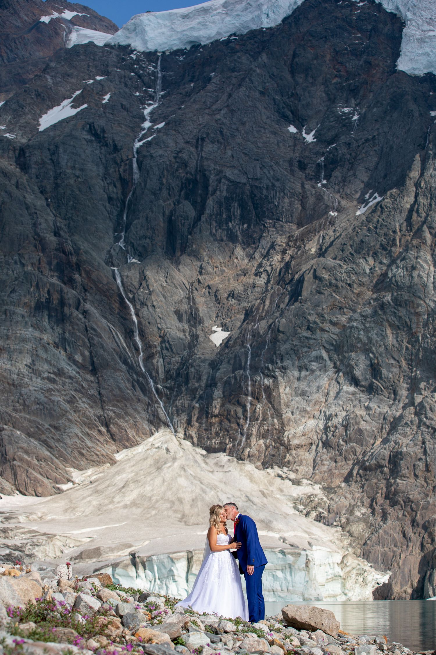 Bride and groom kissing in front of a dramatic mountain glacier landscape during an outdoor wedding ceremony at Lake-of-Hanging-Glacier