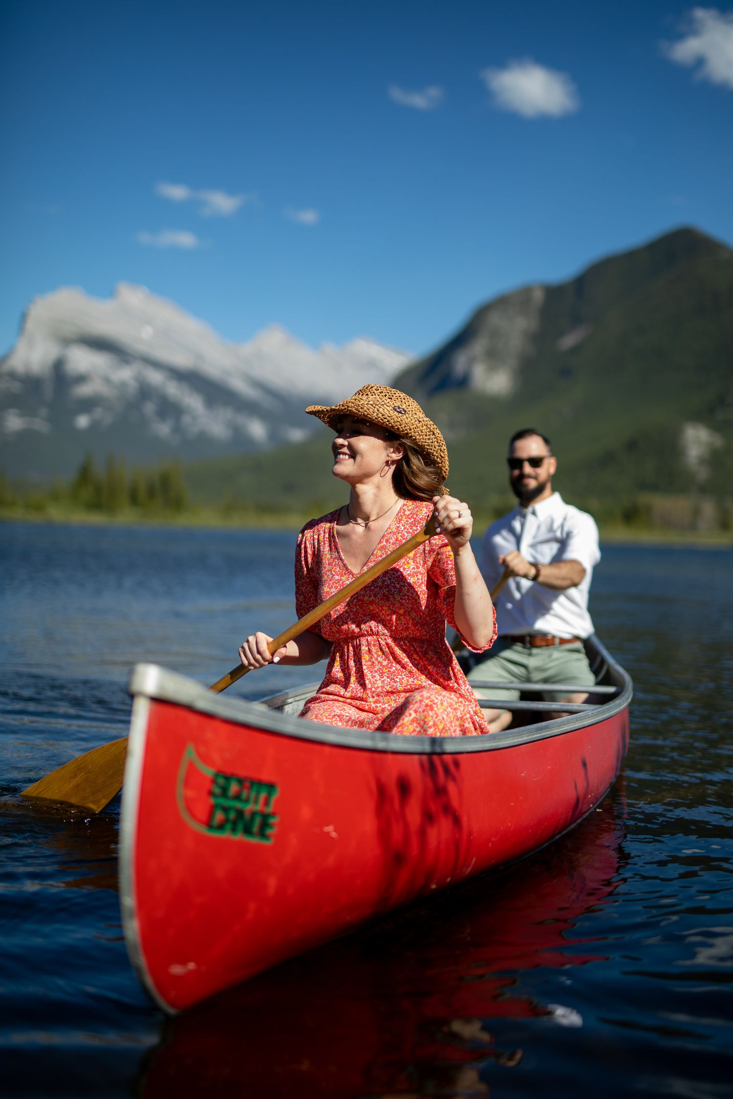 People paddle a red canoe across a scenic mountain lake on a sunny summer day at Vermilion Lakes in Banff.