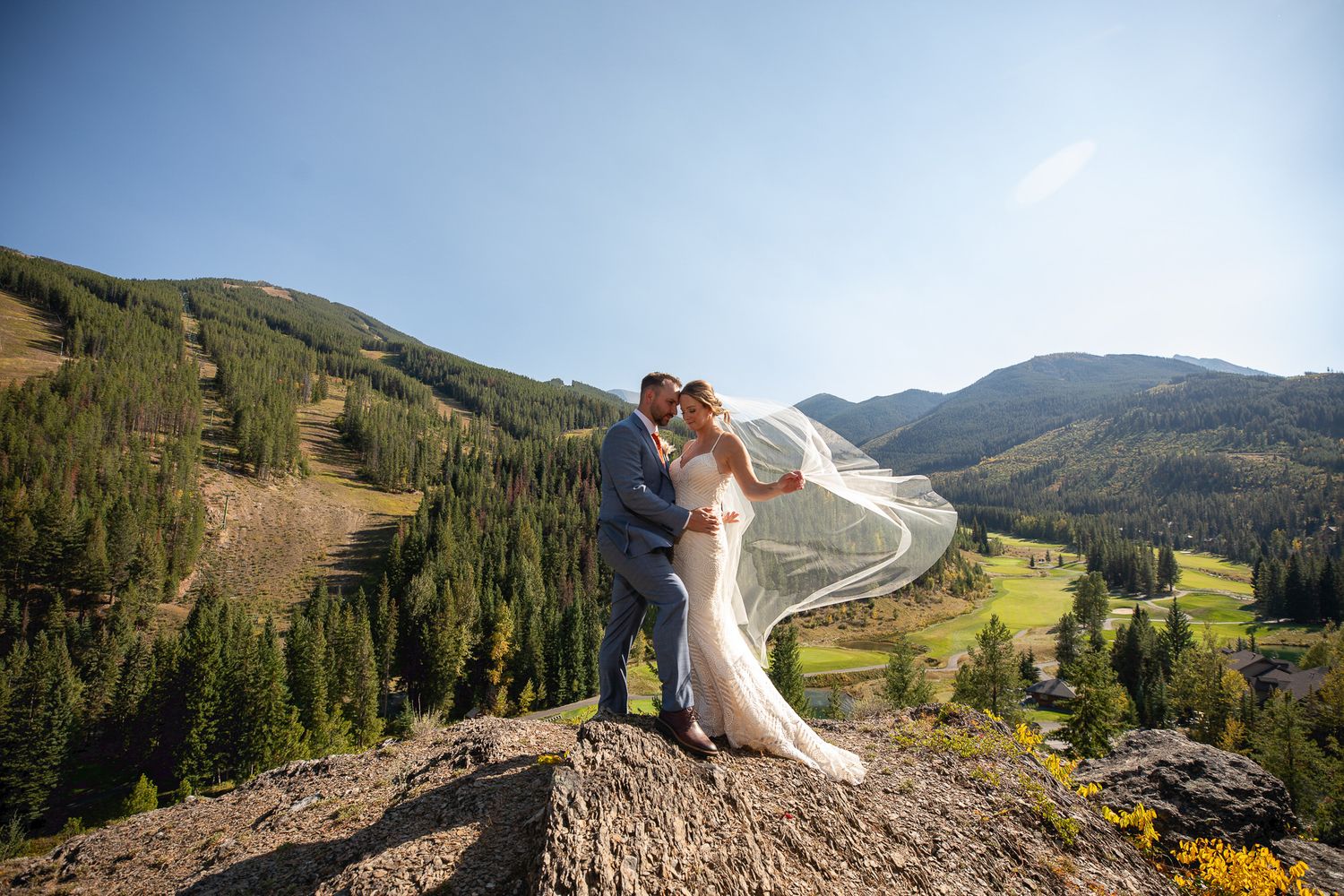 A wedding couple shares a romantic moment on a mountain peak overlooking a scenic valley during their wedding day in Panorama, BC.