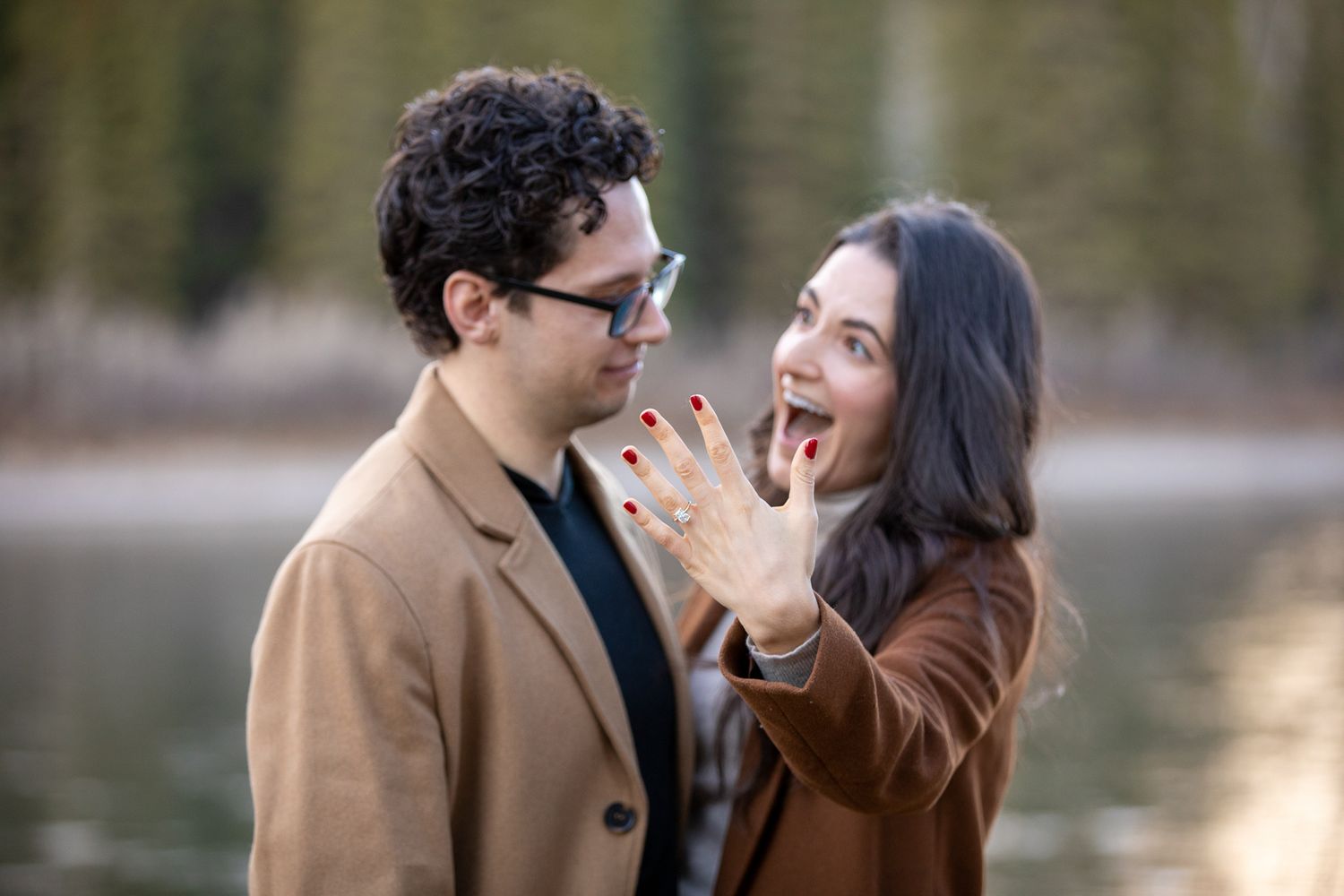 A romantic couple in winter coats share tender moments by a lake during an engagement photo session  in Canmore, AB.