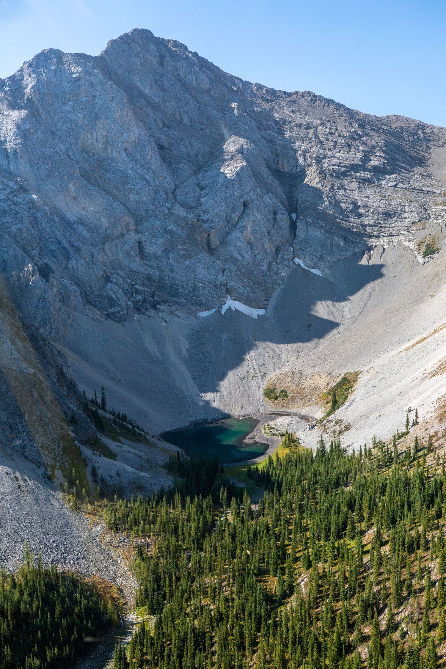 Aerial view of a turquoise alpine lake nestled in a rocky mountain cirque surrounded by evergreen forest in Kananaskis, Alberta.
