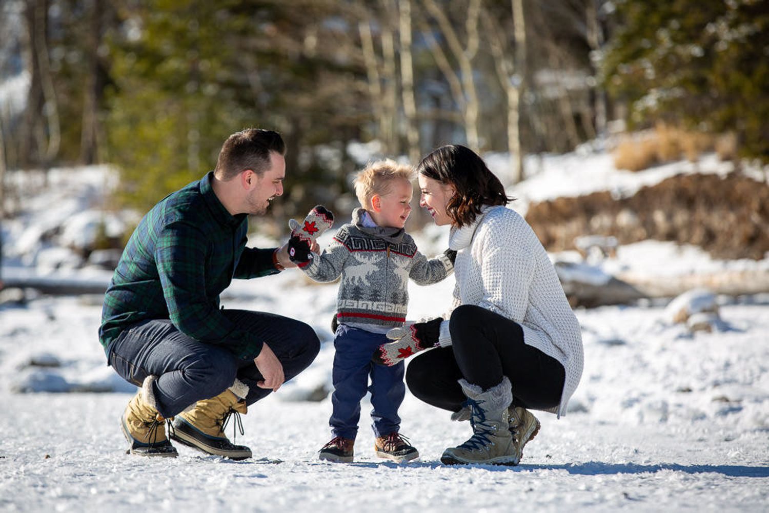 A family plays together in a snowy winter landscape with trees in the background at Minnewanka Lake in Banff, AB.