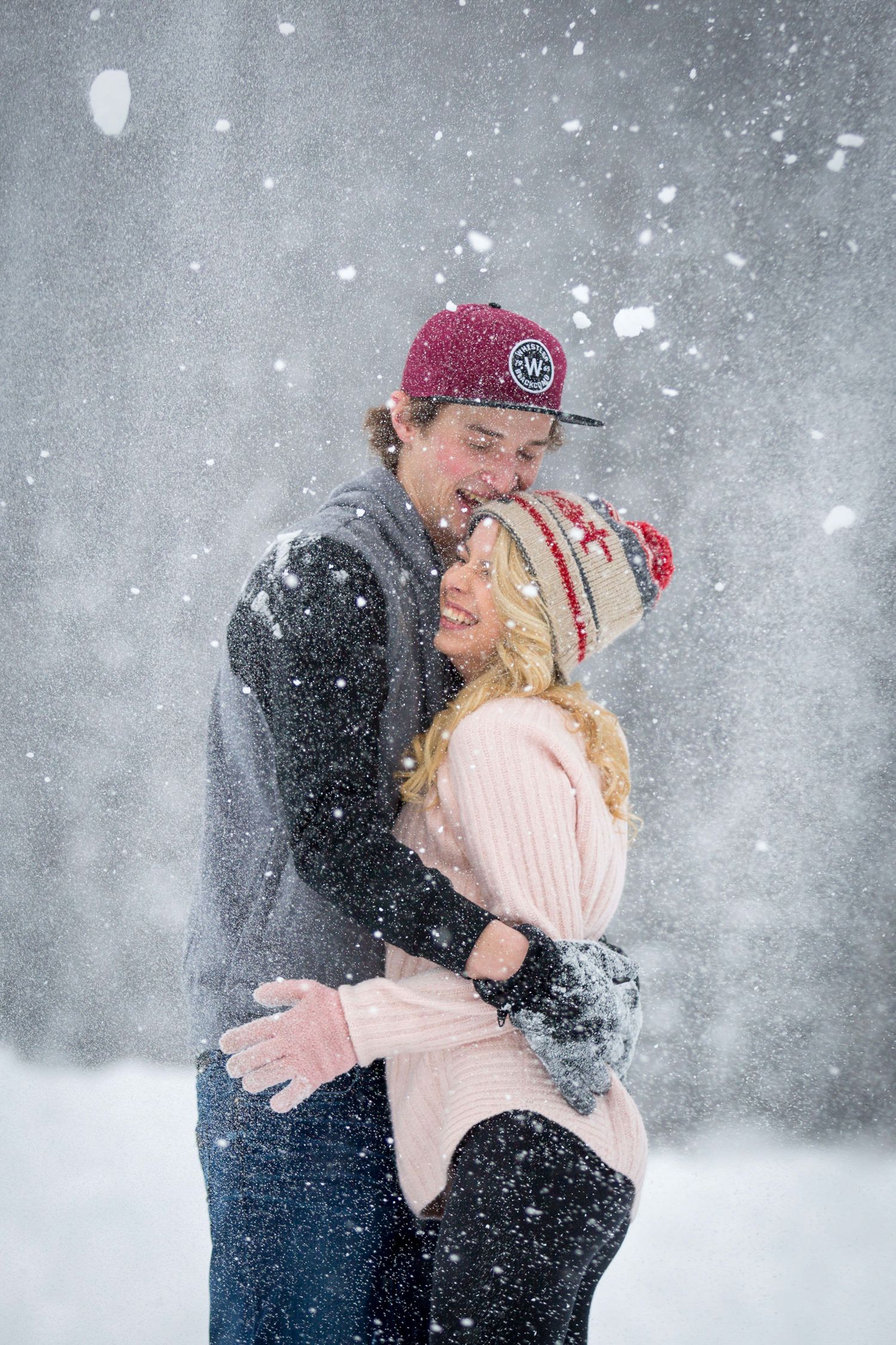 A romantic couple embraces in the falling snow while wearing winter clothing and sharing an intimate moment together at Lake Louise, AB