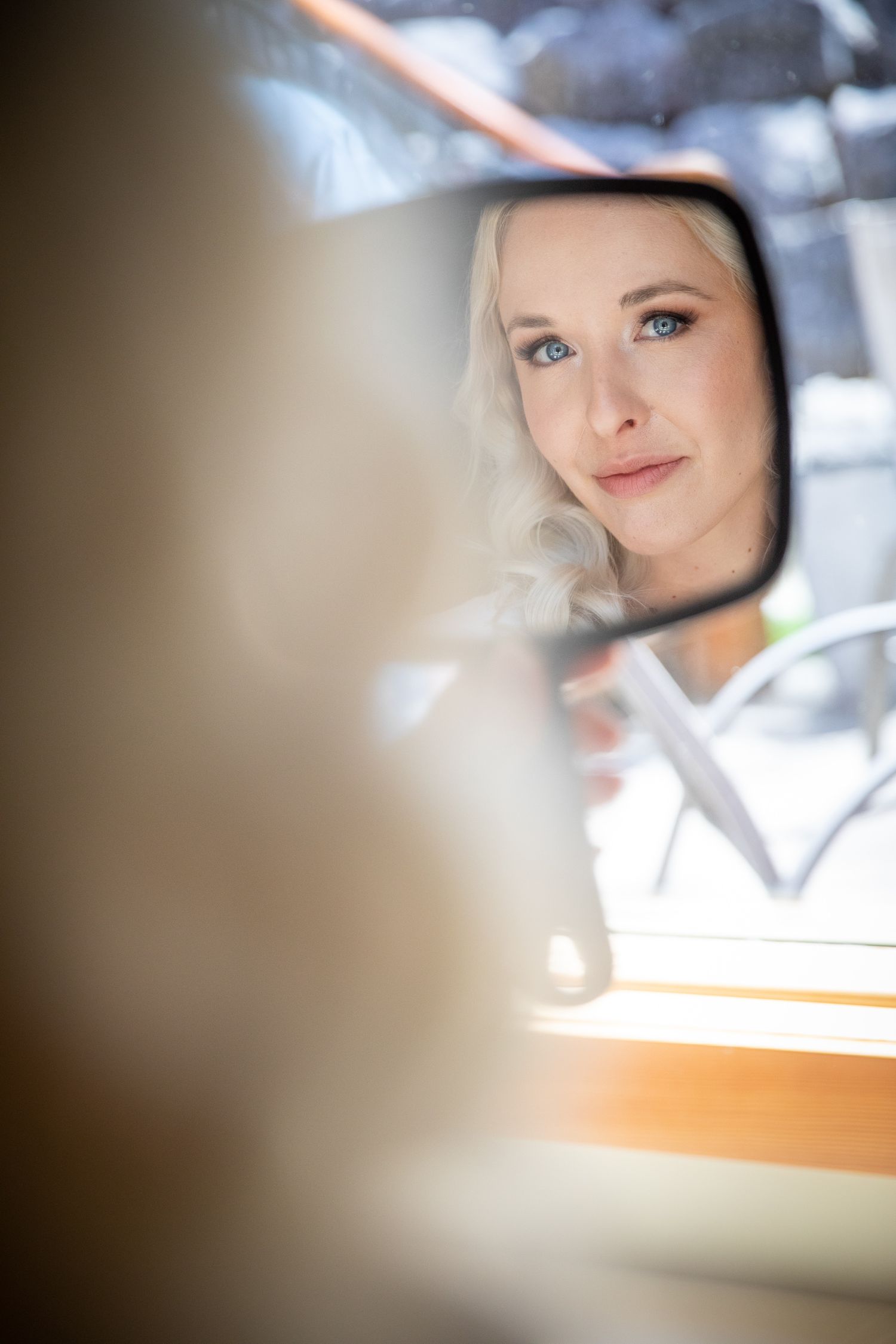 Blonde woman with blue eyes reflected in a vintage car side mirror, gazing thoughtfully into the distance In Canmore