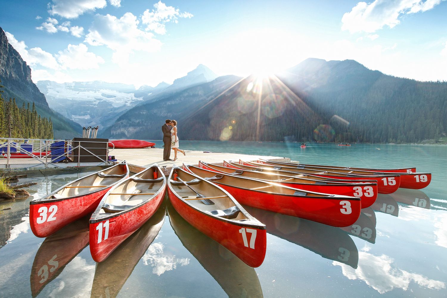 Red canoes lined up at Lake Louise dock with sunburst over Canadian Rocky Mountains in Banff National Park.