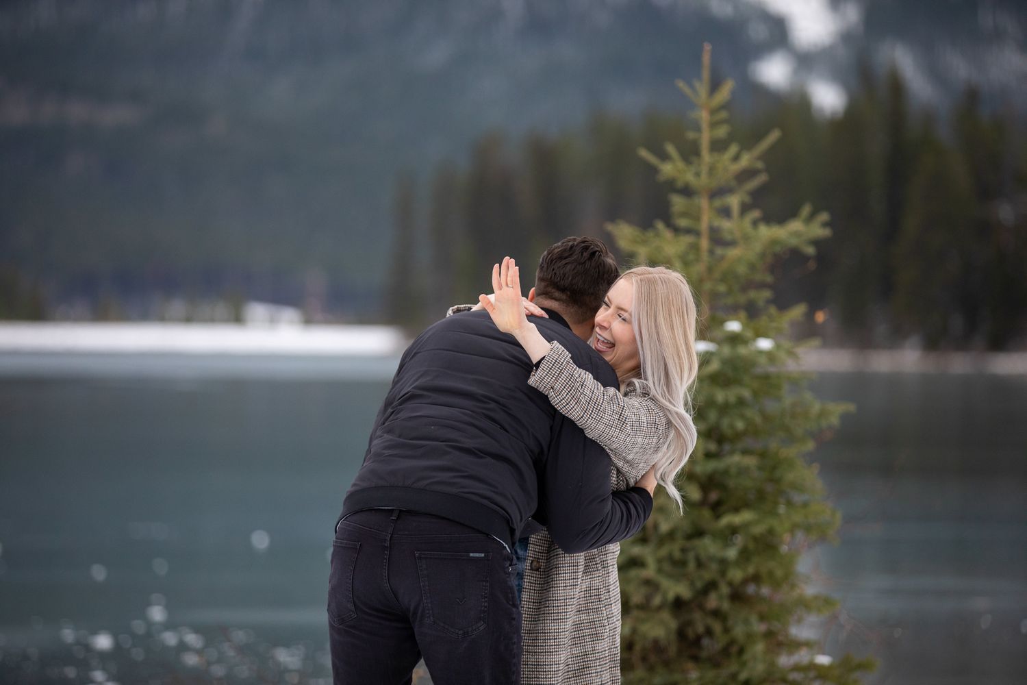 Romantic couple embraces near a misty mountain lake surrounded by evergreen trees and fog in Canmore quarry lake.