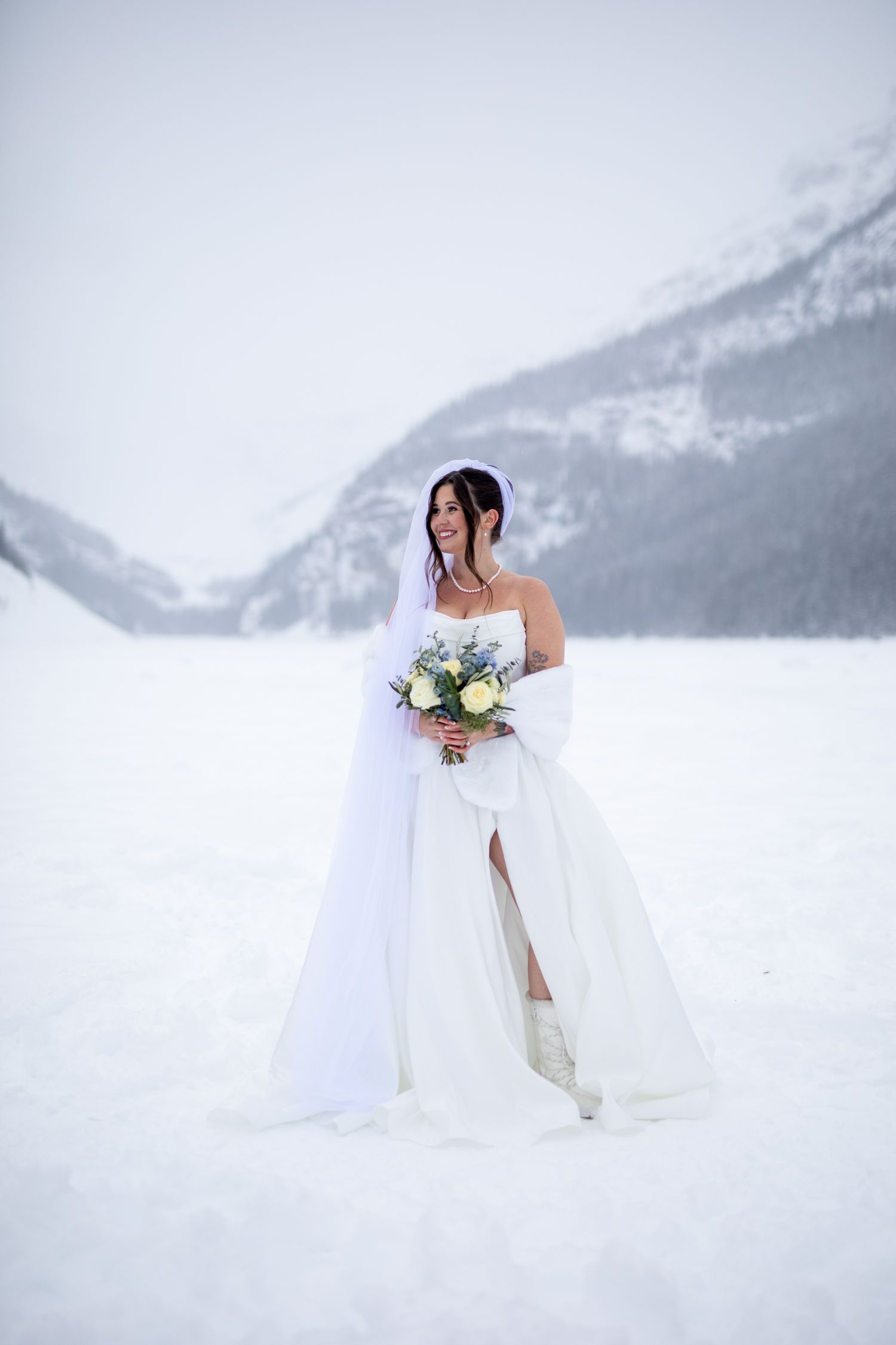 A bride poses for a portrait photos in the pristine snow at Lake Louise with mountains behind her.