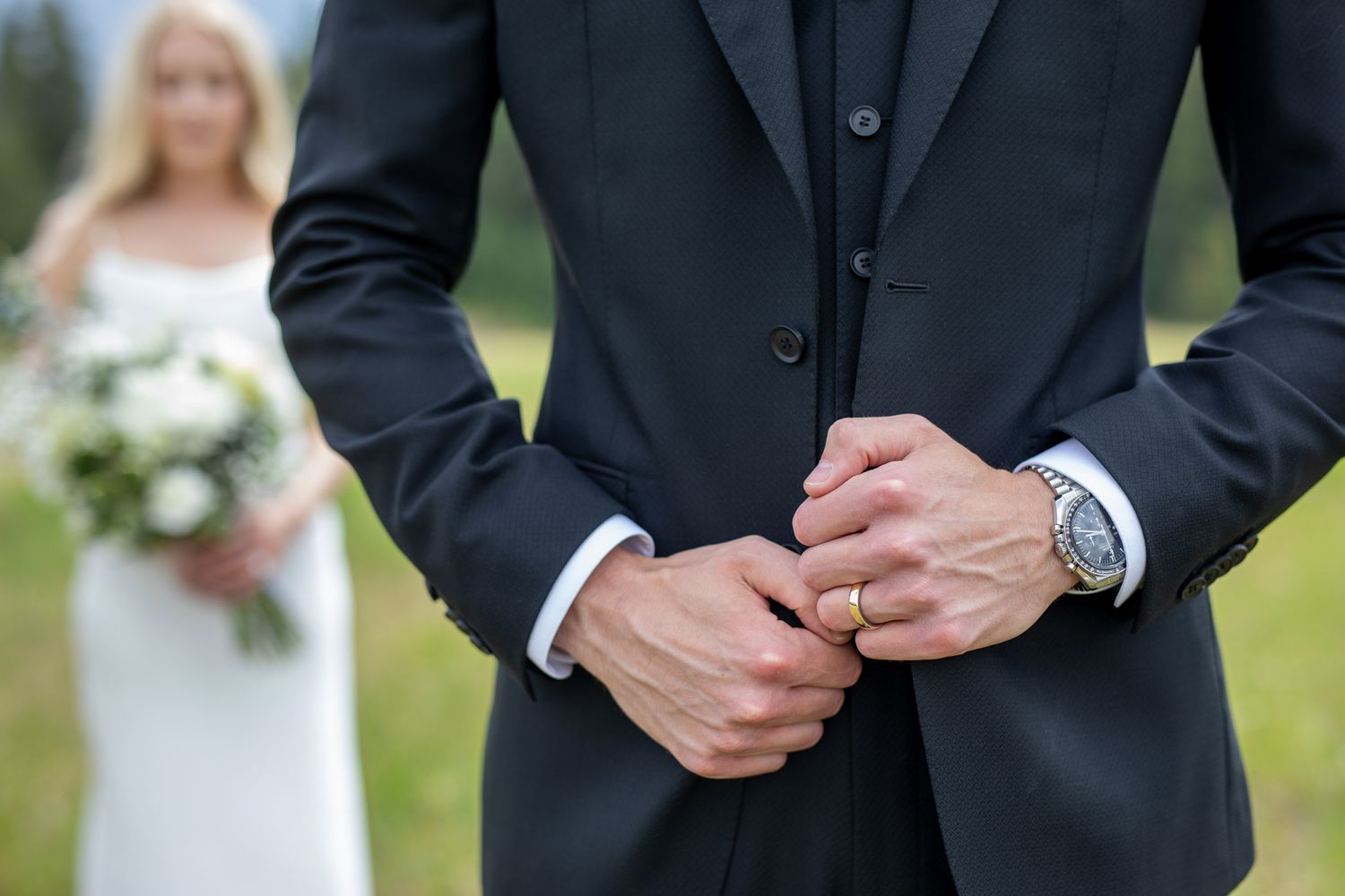 Close-up of groom adjusting cufflinks with bride holding white bouquet in soft focus background. Buffalo Mountain Lodge, Banff, Alberta.