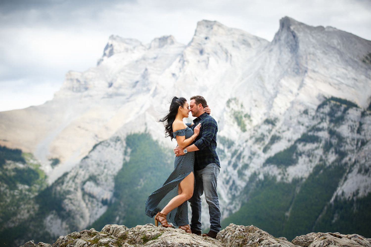Silhouetted couple embraces against dramatic mountain backdrop during sunset in scenic mountain landscape of Lake Minnewanka in Banff.