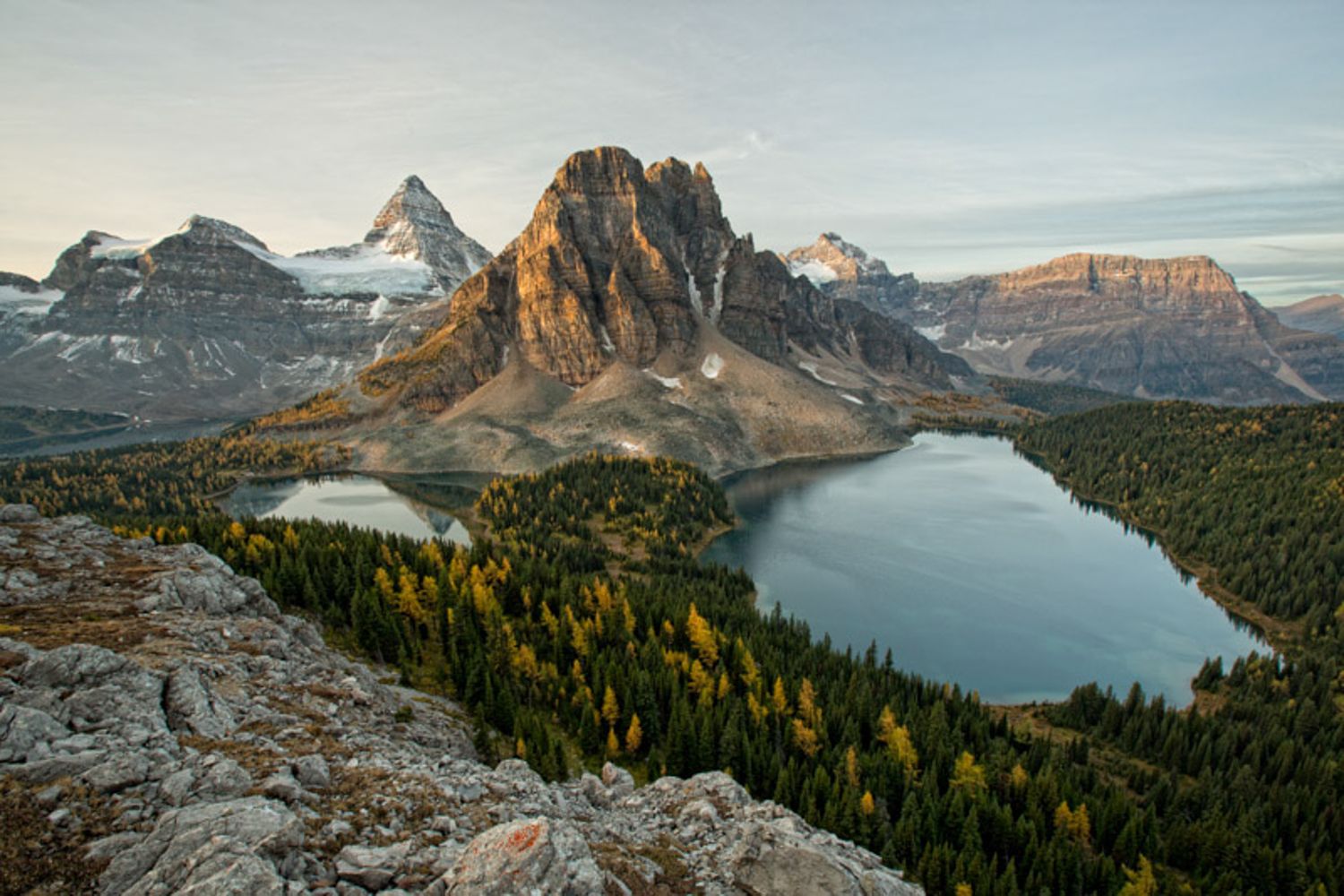 Mount Assiniboine towers over Sunburst Lake and Sunburst Lake in the Canadian Rockies during golden sunset light.