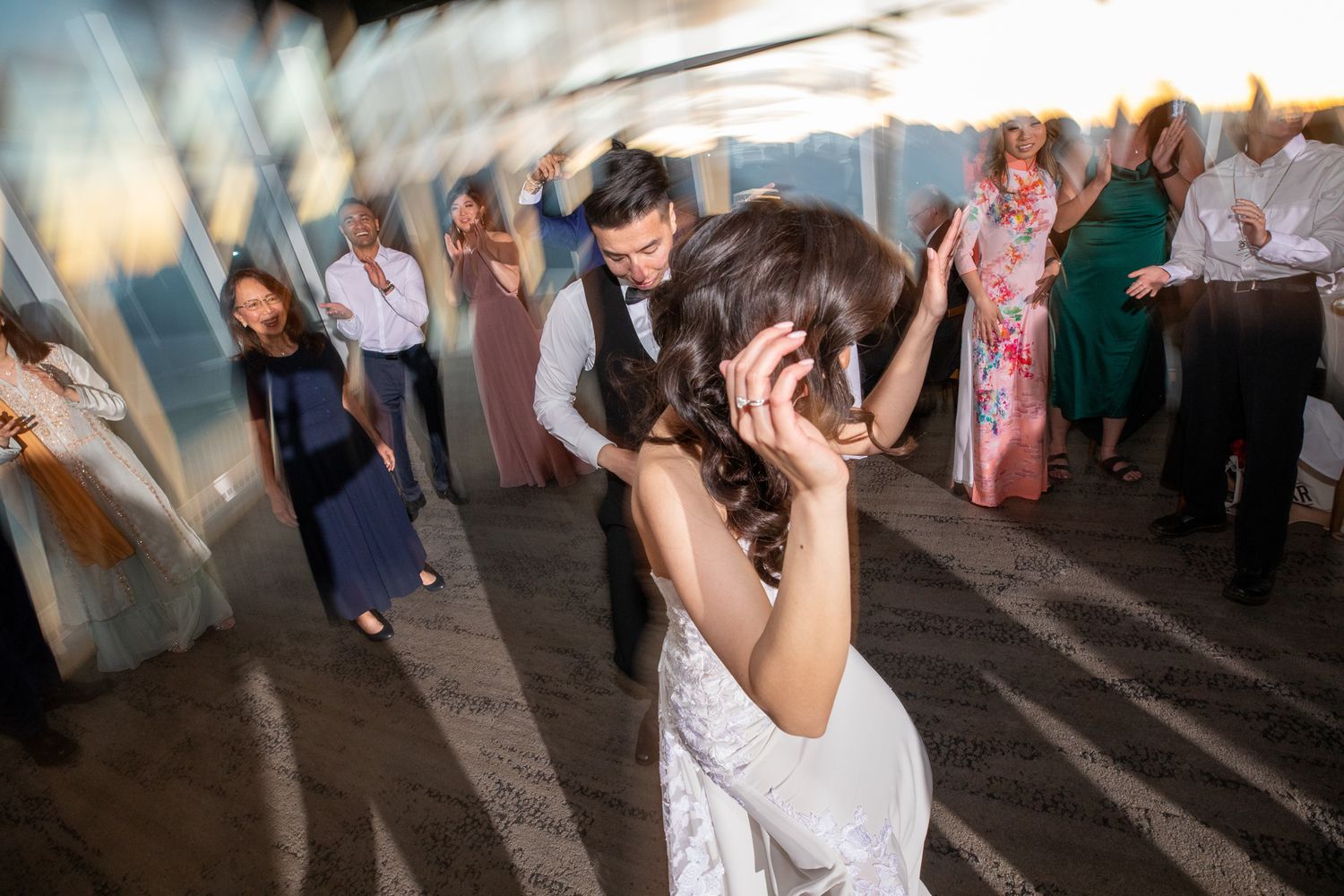 Bride and groom share a romantic dance at their wedding reception with guests celebrating in the background at sunset.