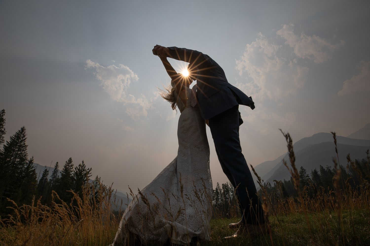 A silhouetted couple dances in a field at sunset with mountains and trees in the background at Grey Wolf golf club in Panorama, BC