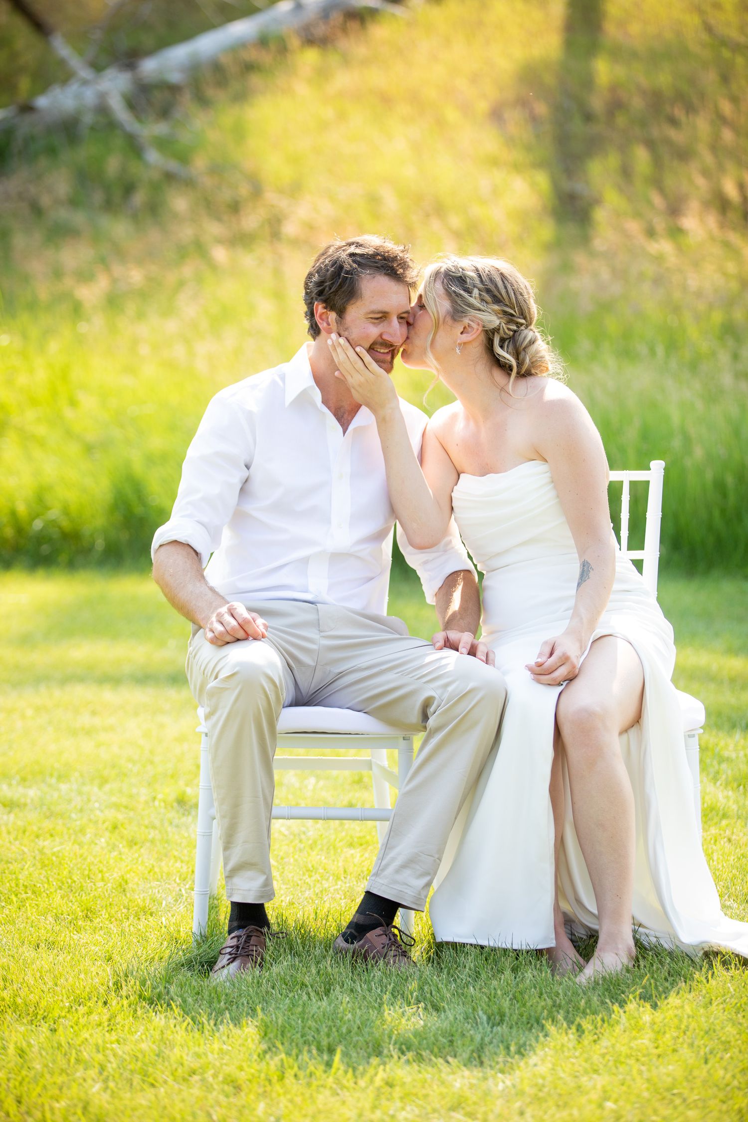 A bride and groom share a romantic moment seated on white chairs outdoors on a sunny green lawn at Swansea Ranch in Invermere, BC