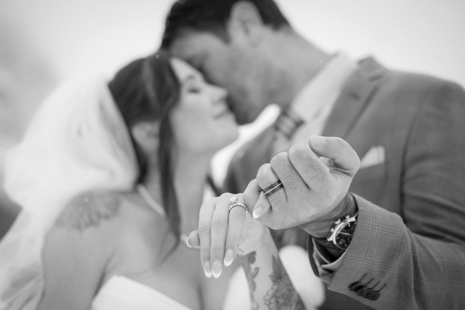A romantic black and white wedding photo showing a close-up of a couple's hands with rings at Lake Louise, Alberta.