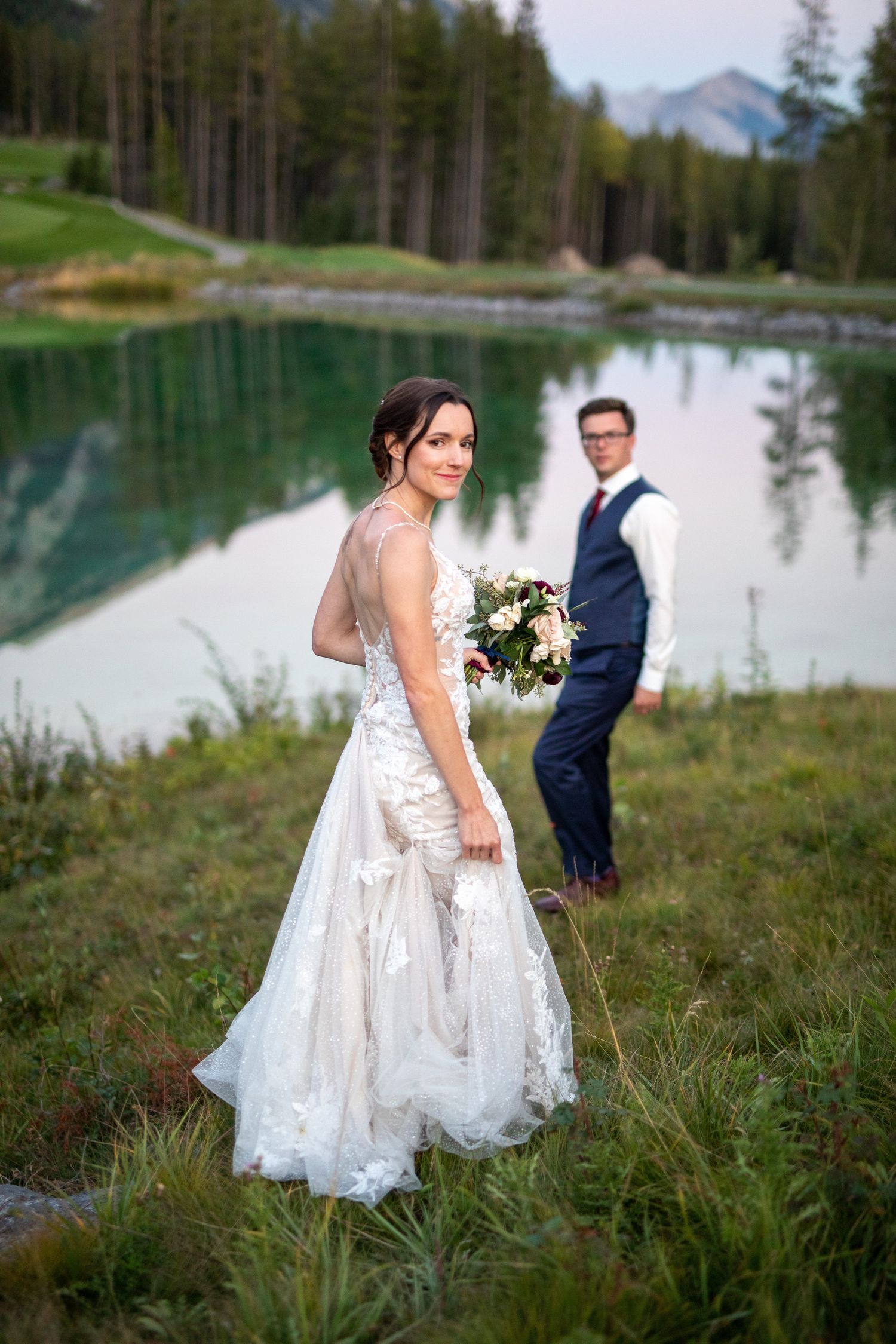 Wedding couple poses by serene mountain lake surrounded by evergreen forest and natural landscape at Silvertip Resort in Canmore, AB.