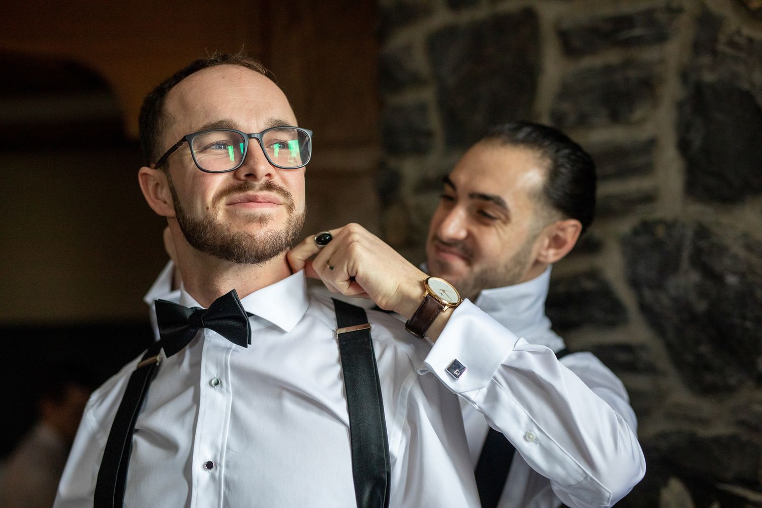 A wedding party member in a white dress shirt and suspenders adjusts his collar and cuffs before the ceremony.