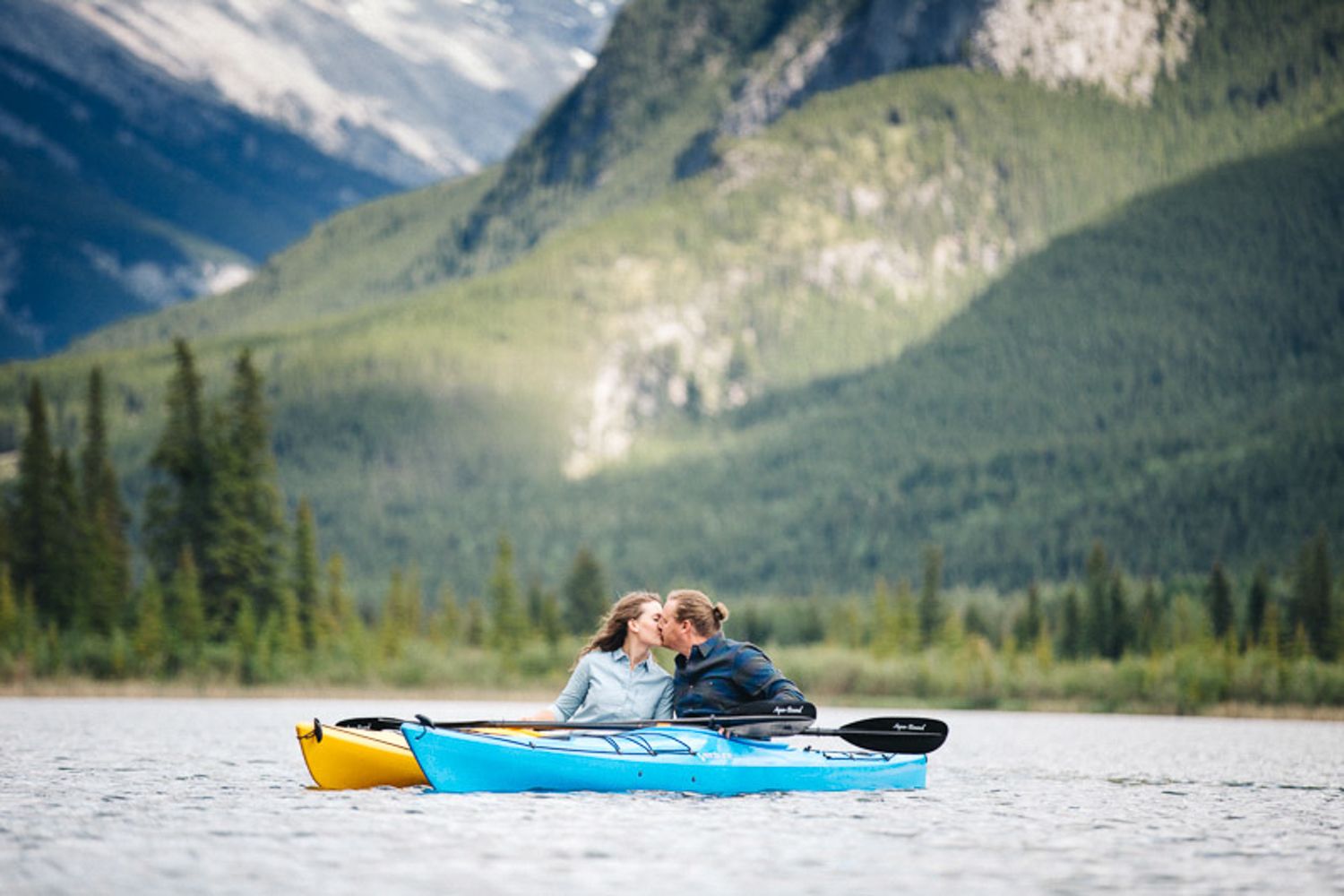 Kayakers paddling on a serene mountain Vermilion lake surrounded by snow-capped peaks in Banff National Park.