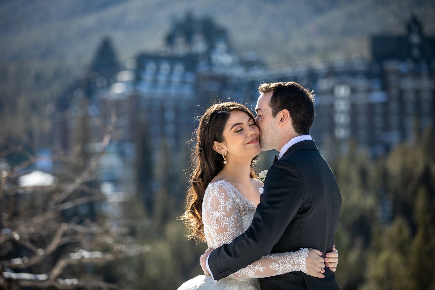 A romantic wedding couple embraces in front of the majestic Banff Springs Hotel on their winter wedding day.