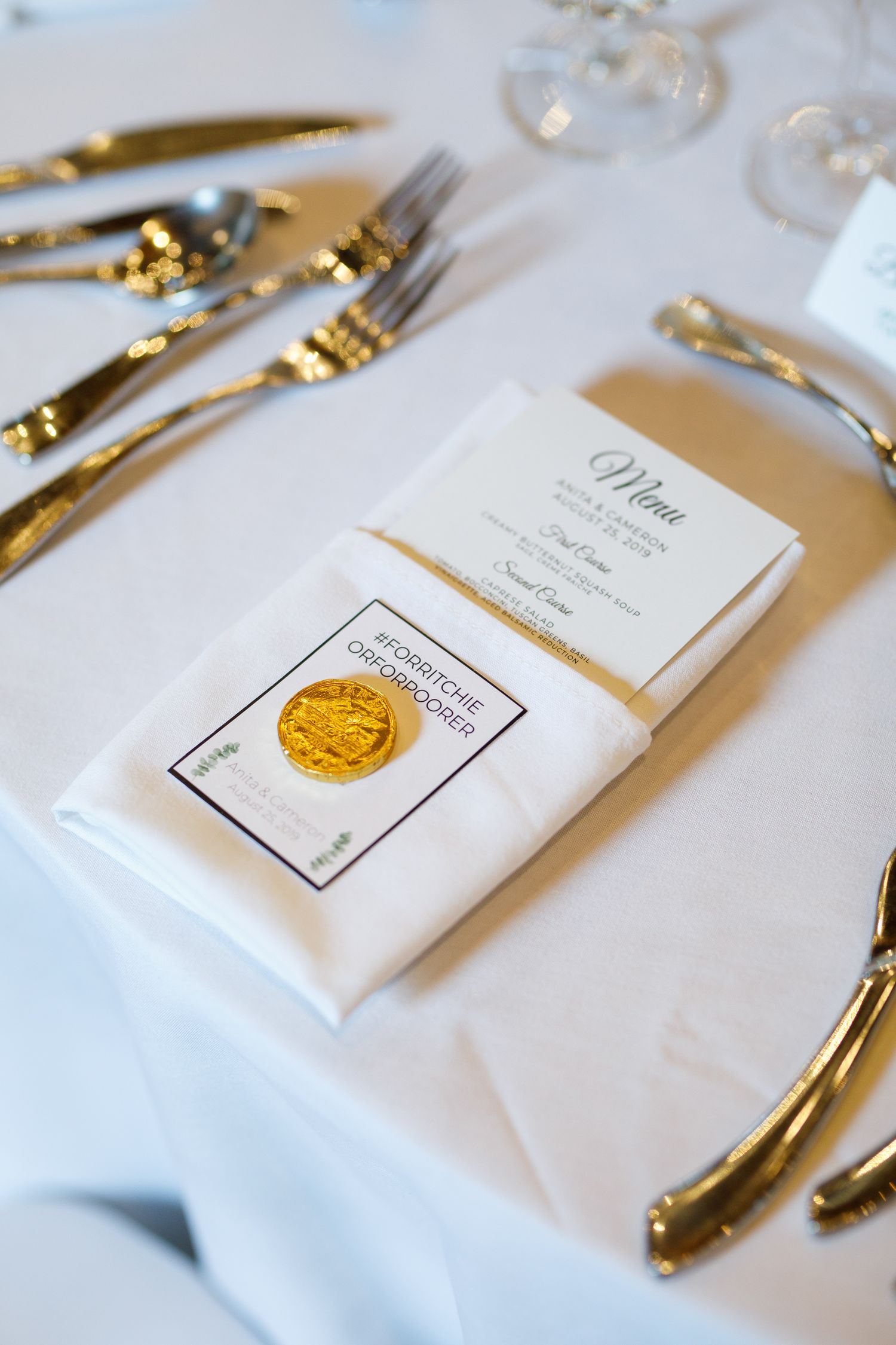 Elegant place setting with gold-trimmed silverware and white menu cards on crisp white tablecloth.