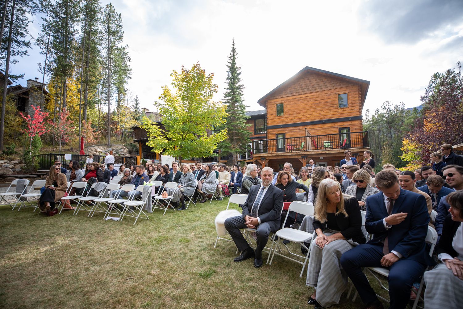Outdoor wedding ceremony seating arrangement with wooden chairs facing a forest backdrop and rustic cabin. Earl Grey Lodge Panorama BC