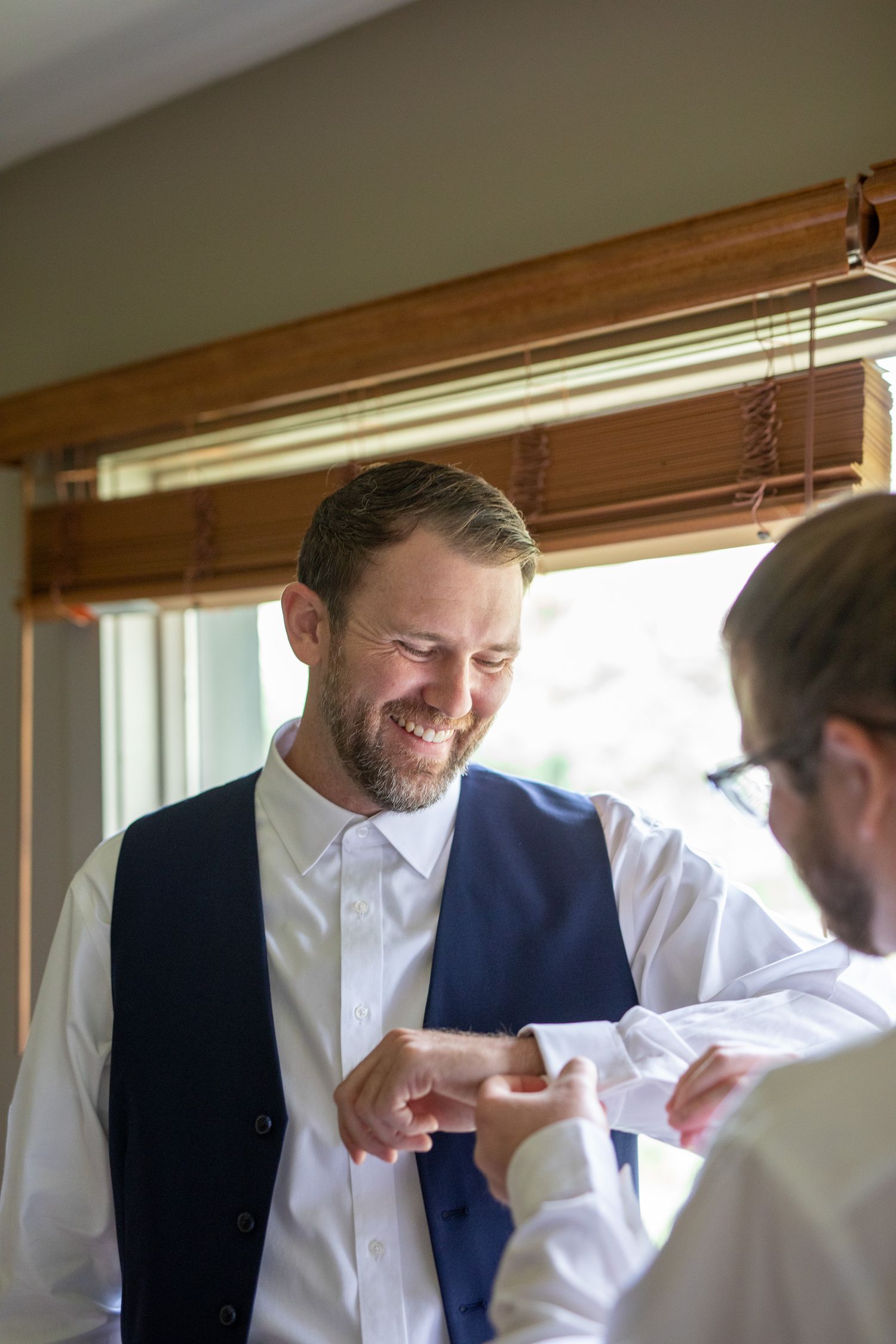 A person in a white dress shirt and navy vest smiles while getting ready in front of a window. Buffalo Mountain Resort, Banff.