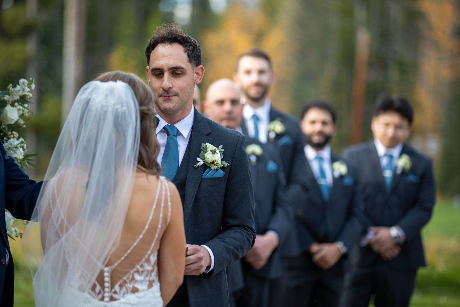 Wedding party in navy blue suits and white dress gather outdoors at the gazebo venue at Silvertip resort in Canmore, AB.