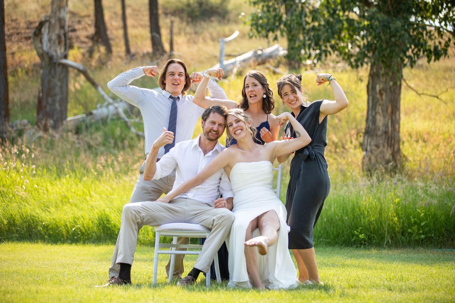 Wedding party posing joyfully outdoors on green grass, bride in white gown with friends celebrating in sunny natural at Swansea Ranch