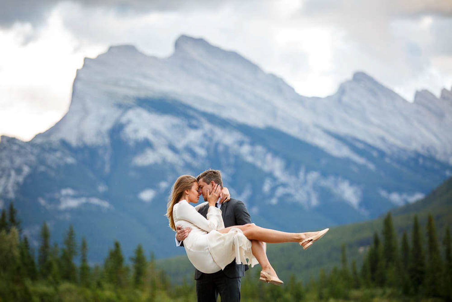 A couple embraces in front of majestic Mount Rundle snow-capped mountains in Banff National Park.