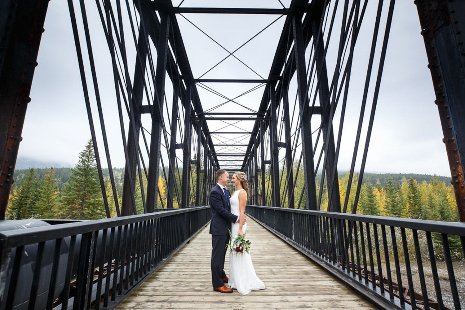 A couple shares a romantic moment on a steel bridge walkway overlooking scenic mountain views. Old engine bridge in Canmore, Alberta.
