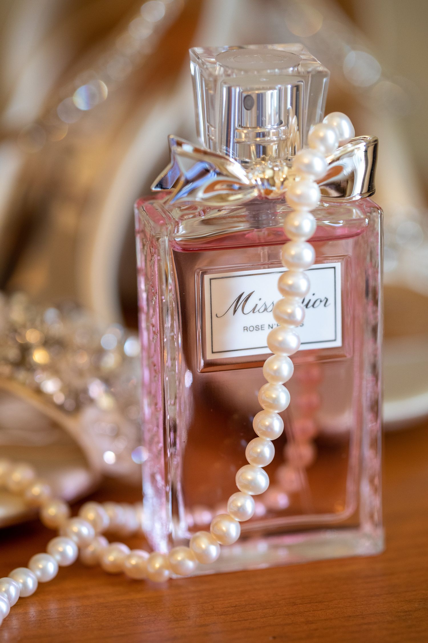 Miss Dior Rose perfume bottle adorned with pearl necklace on wooden surface with elegant accessories In Canmore