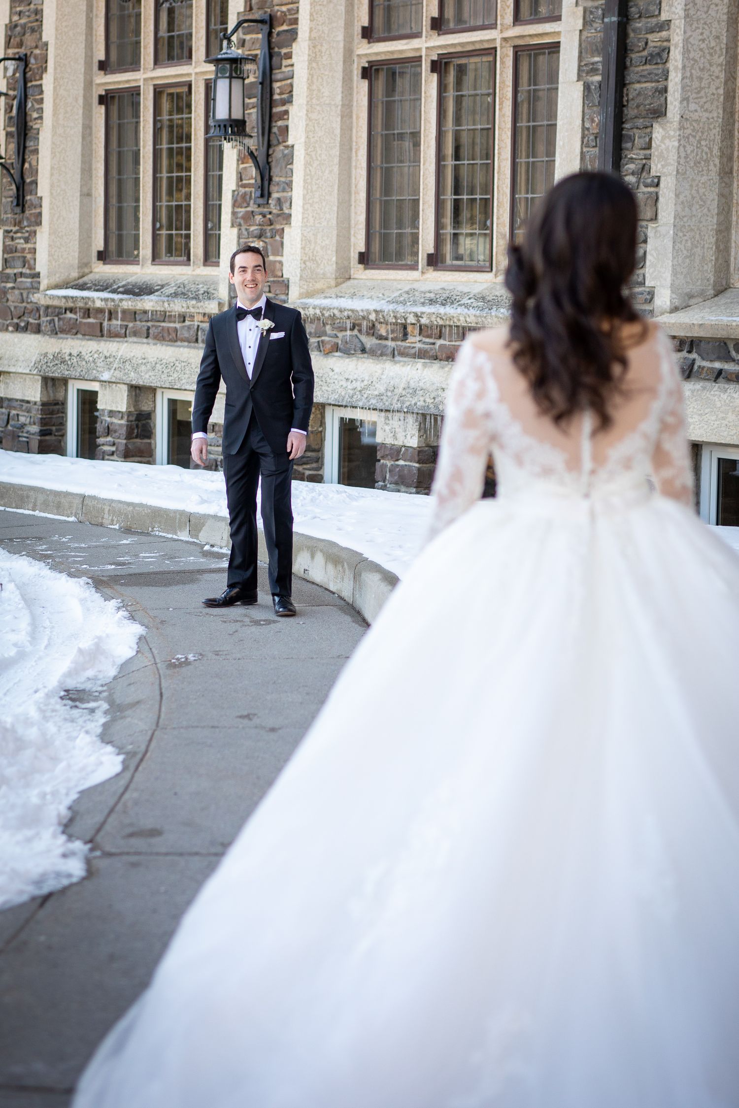 A bride in a flowing white gown twirls on a stone patio while a suited figure watches from a distance. Fairmont Banff Springs Hotel
