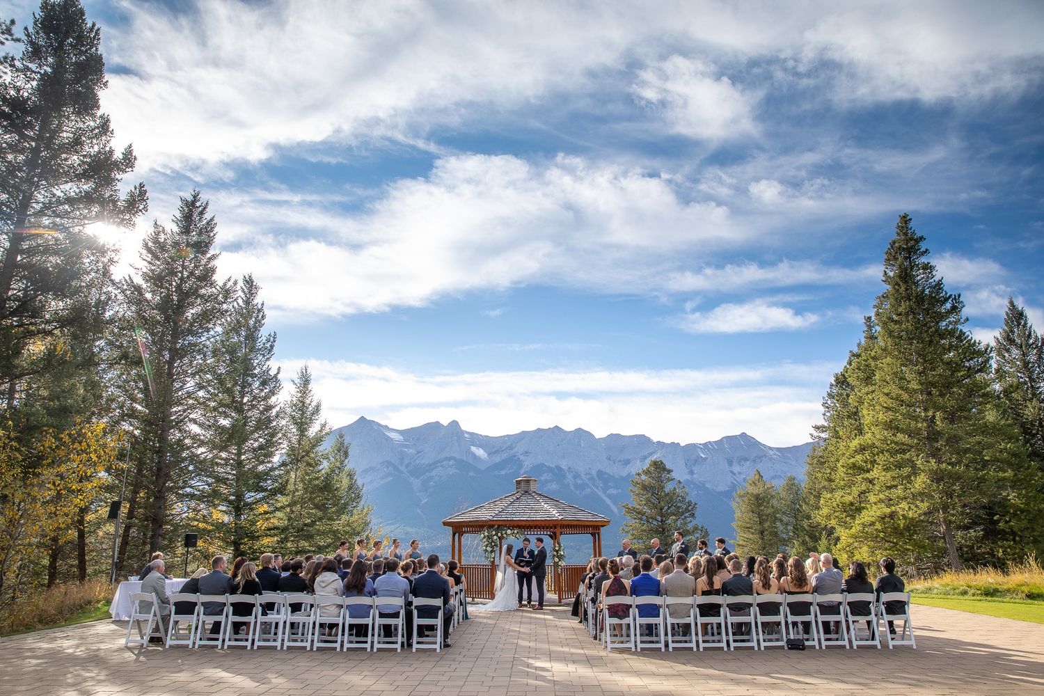Outdoor Silvertip gazebo wedding ceremony setup with white chairs and wooden arch overlooking scenic mountain peaks and blue sky in Canmore.