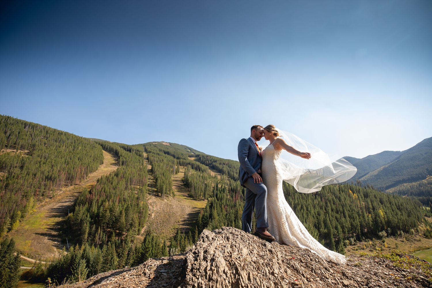 A wedding couple shares a romantic moment on a mountain peak overlooking a scenic valley during their wedding day in Panorama, BC.