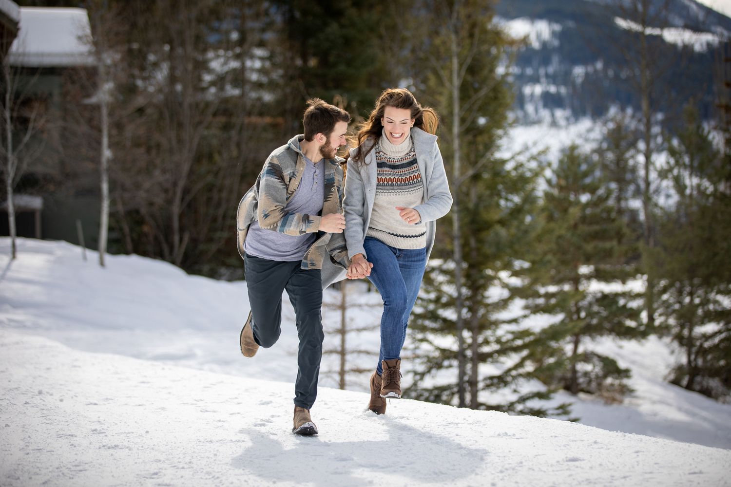 A couple walks together through a snowy winter landscape while holding hands and enjoying the mountain scenery at Grey Wolf Panorama, BC