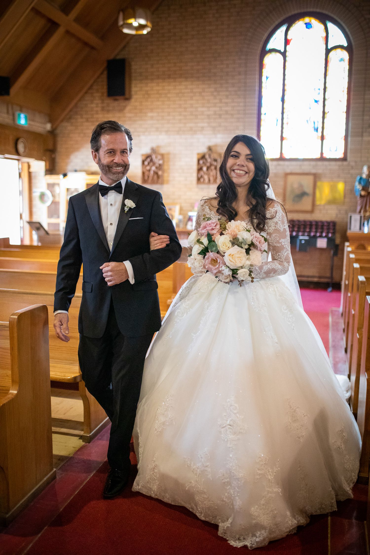A bride and groom walk down the aisle of a church, the bride wearing a white wedding dress and the groom wearing a black tuxedo Banff