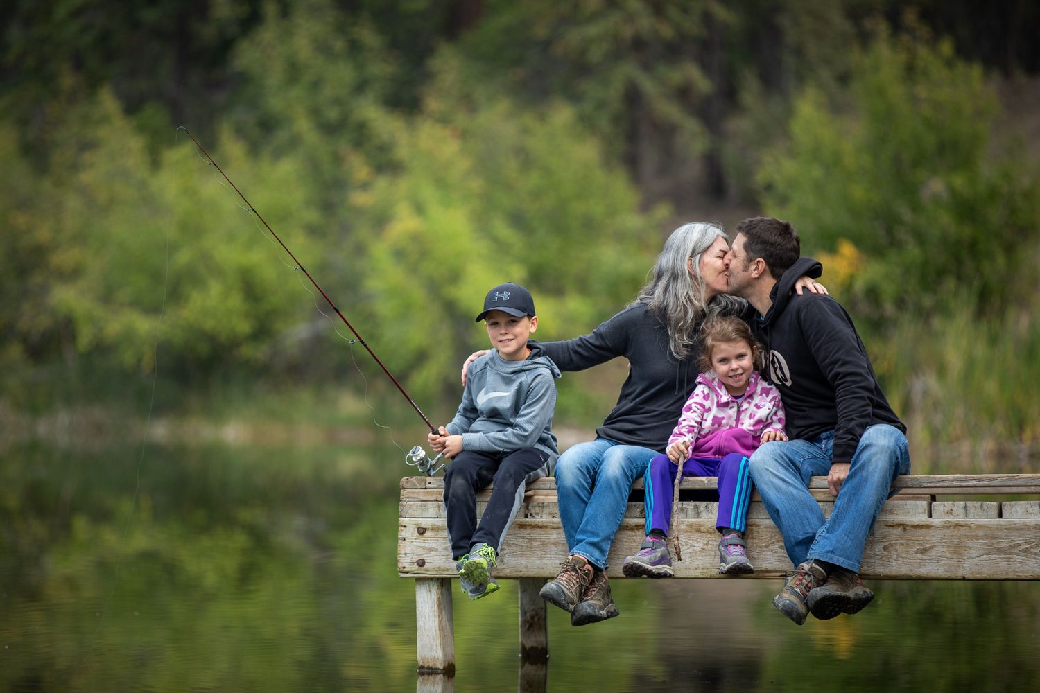 Family sitting together on wooden dock in at Lilian Lake park in Invermere, BC.