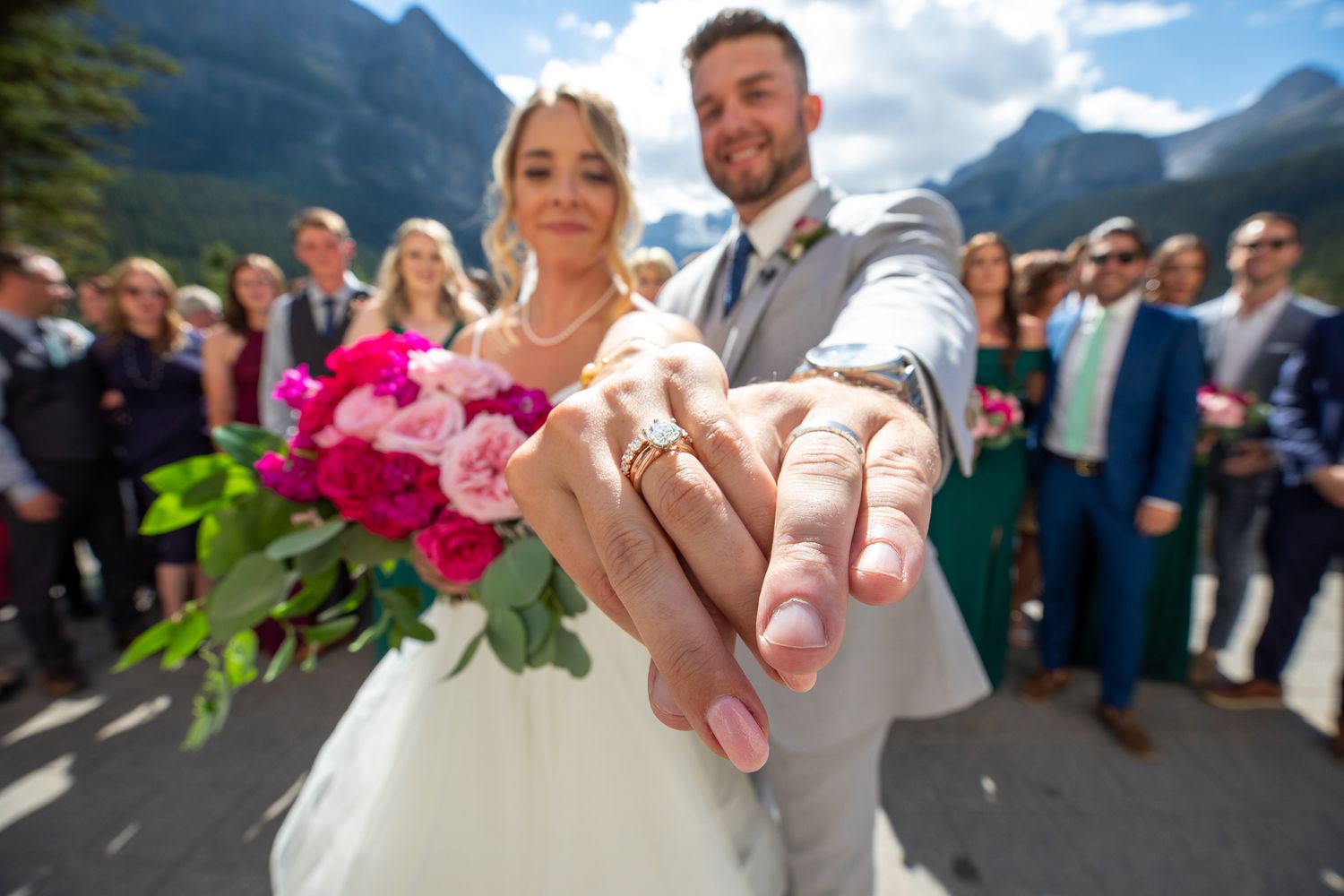 Wedding rings being exchanged against a backdrop of majestic mountain peaks at Lake Louise during an outdoor ceremony.