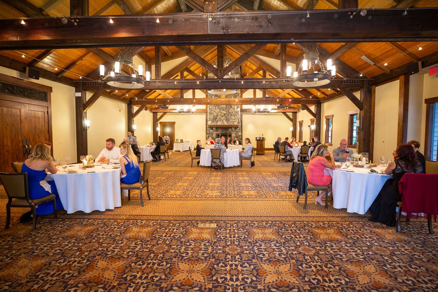 Elegant banquet hall with wooden beam ceiling, chandelier, round tables with white linens, and guests dining on patterned carpet. Silvertip.