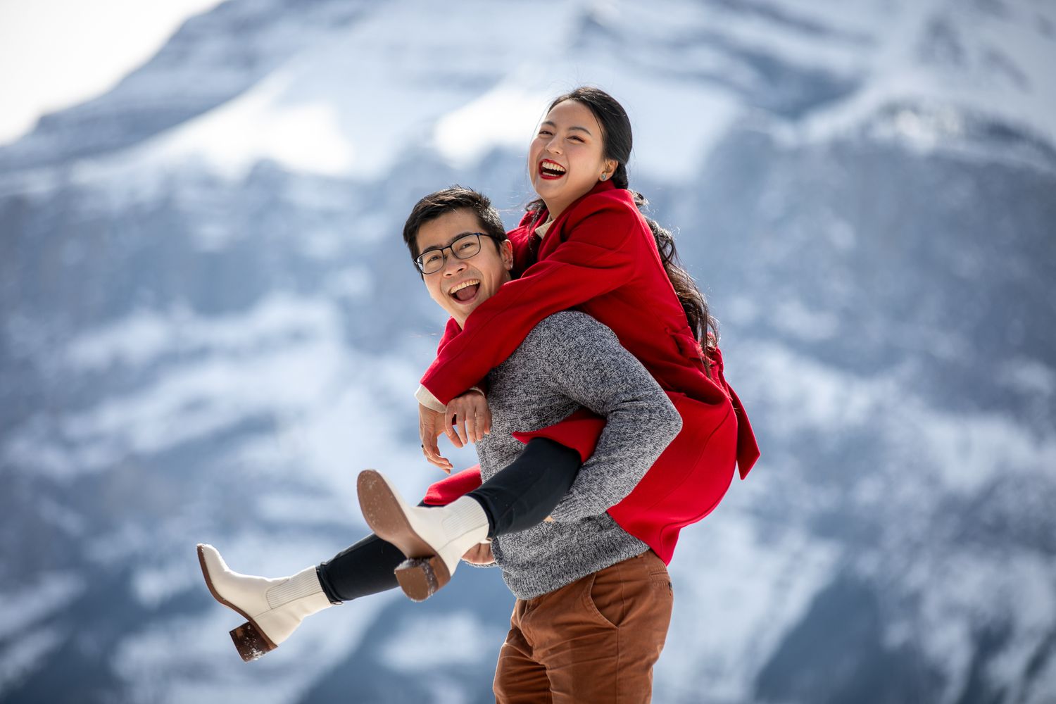 Person in red vest and grey sweater performs playful poses against snowy mountain backdrop  in Banff, AB.