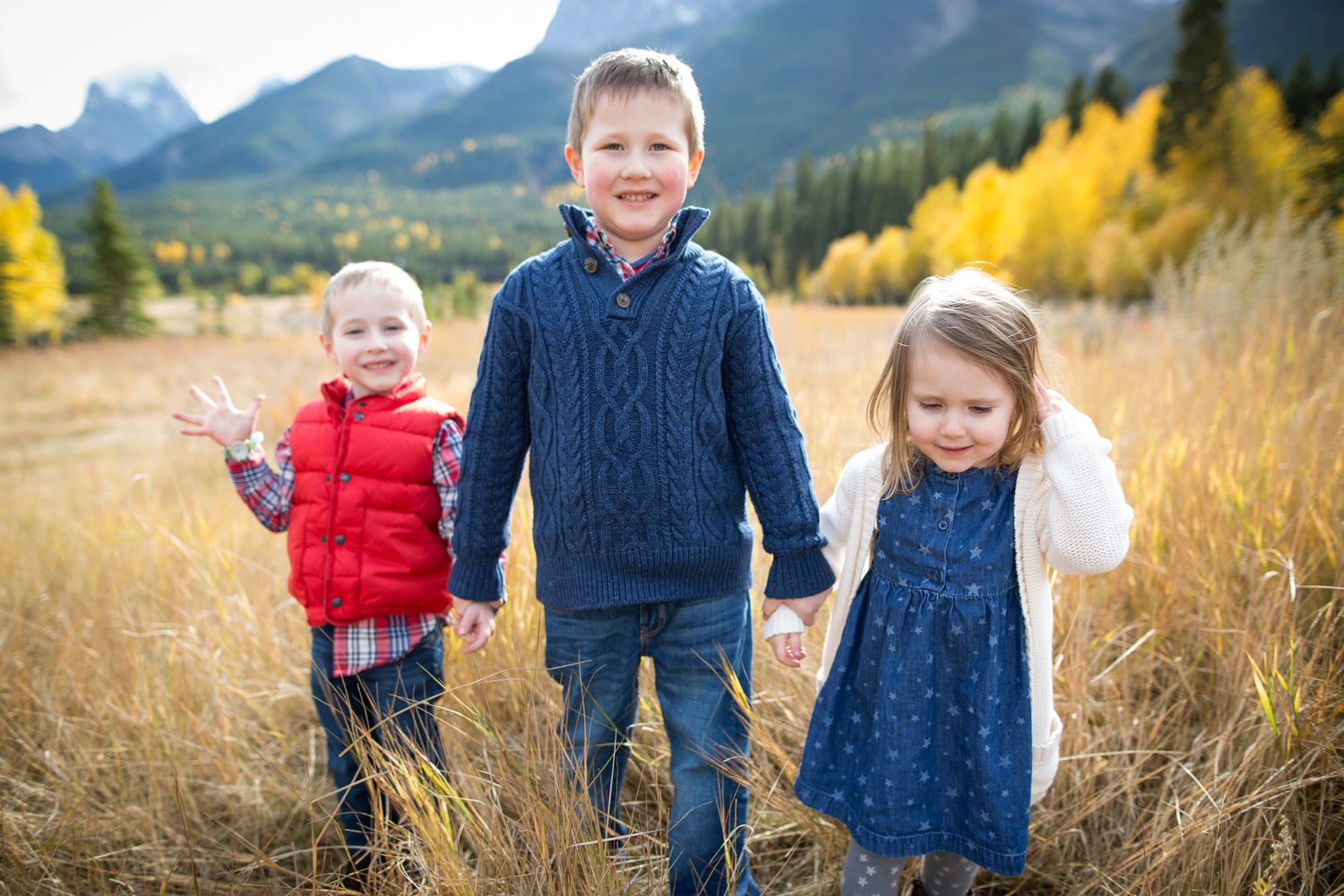 Family enjoying autumn mountain scenery with golden grass and evergreen trees in the background at Quarry Lake Park, Canmore, AB.