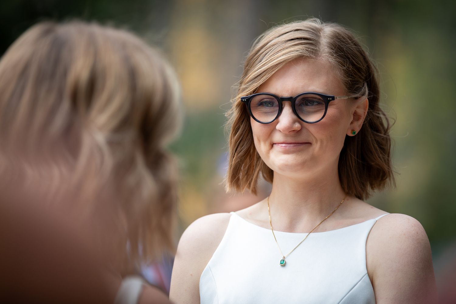 A series of portrait photos showing a person with short brown hair wearing glasses and a white sleeveless top outdoors.