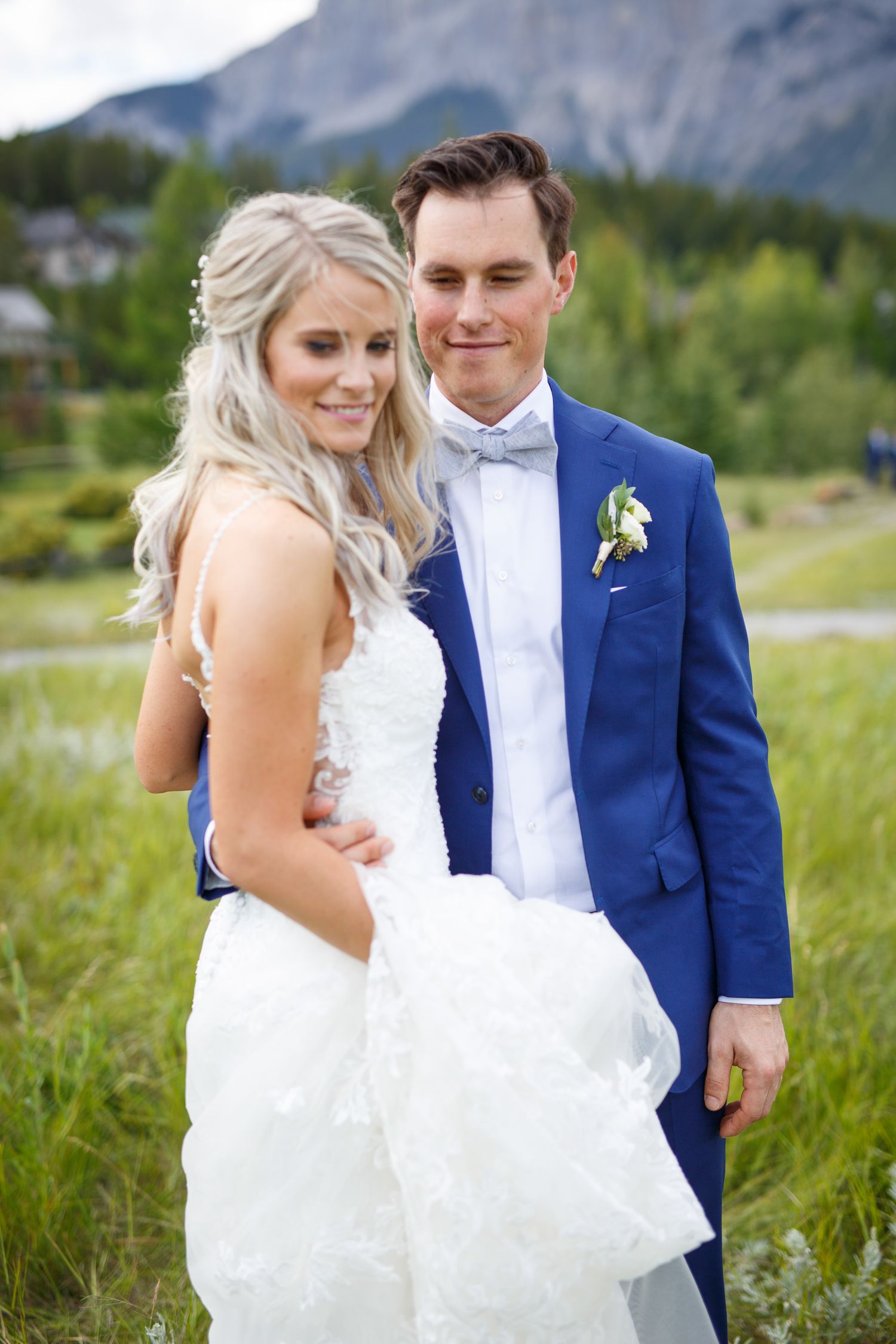 A couple in wedding attire share intimate moments in a mountain meadow with scenic peaks in the background. in Canmore.