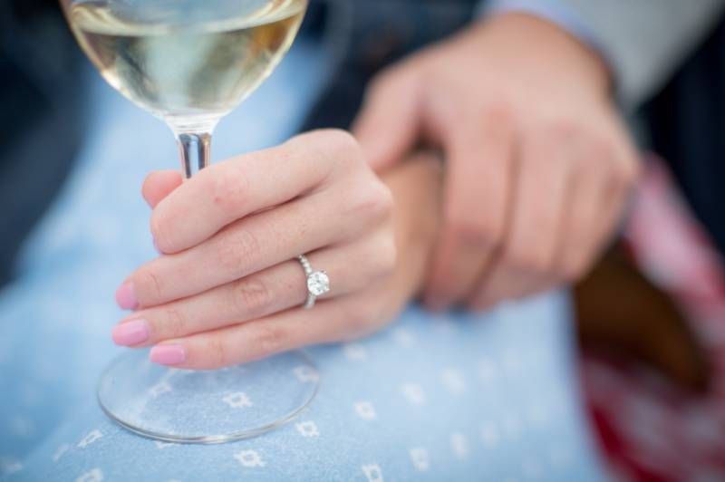 Close-up of an engagement ring on a womans hand holding a glass of white wine at Fish Creek Park in Calgary.
