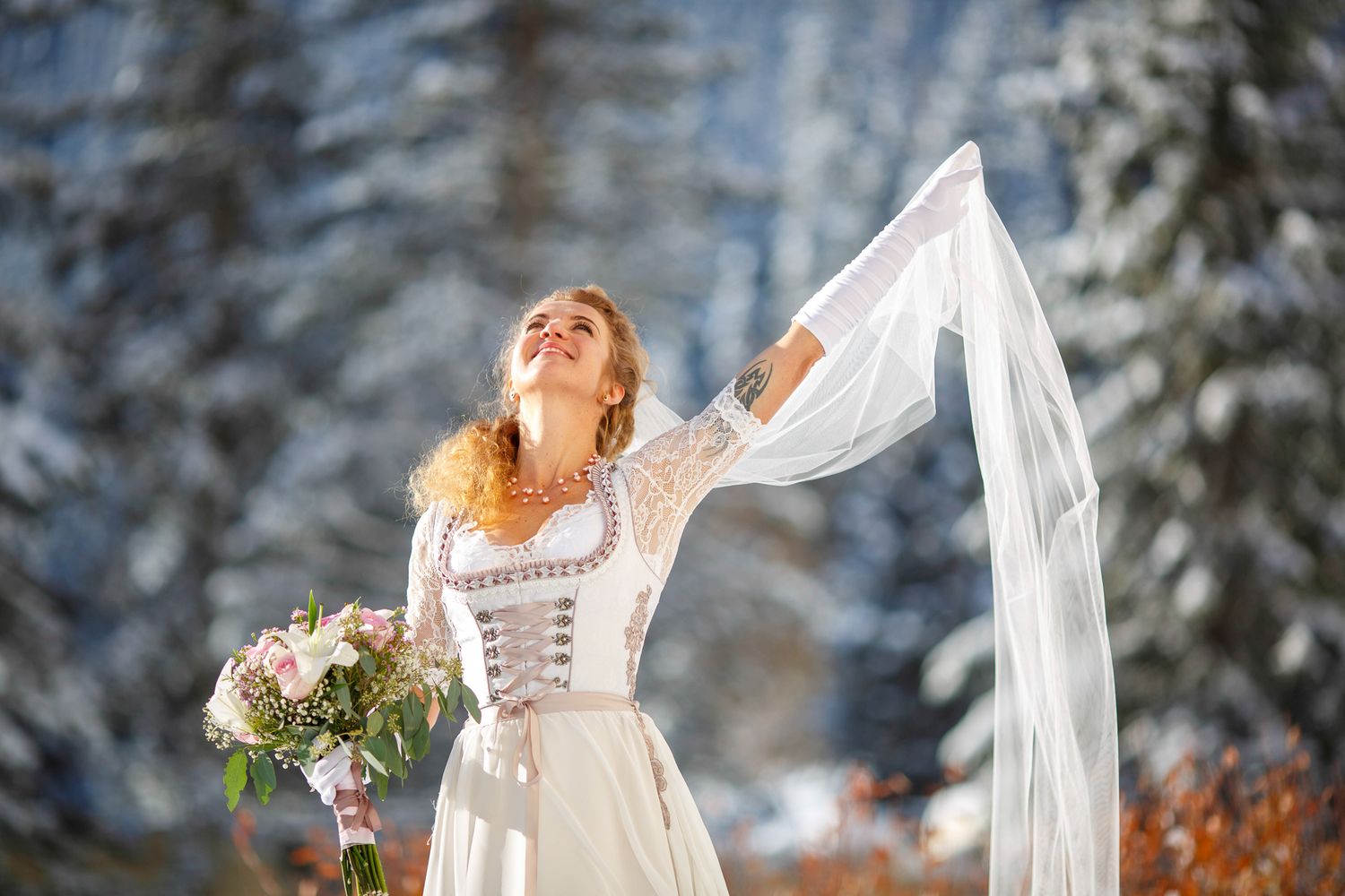 A bride in a white lace dress poses gracefully in a snowy winter forest setting back drop at Lake Louise.