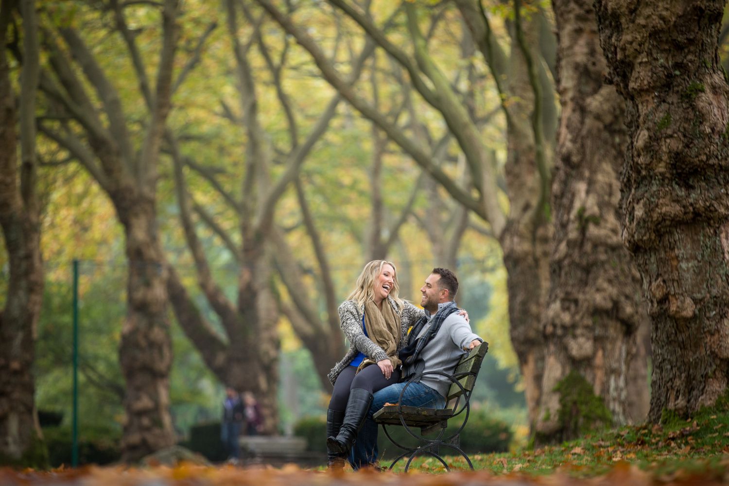 A couple embraces and laughs together in a romantic autumn park setting surrounded by tall trees in Stanley Park in Vancouver, BC.
