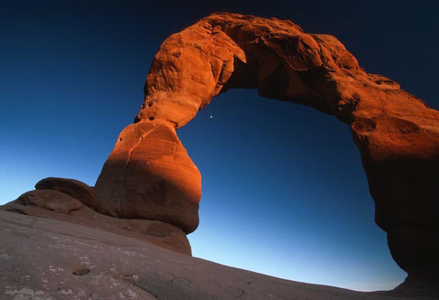 Dramatic time-lapse sequence showing the changing light on a sandstone arch formation in Arches National Park at sunset.