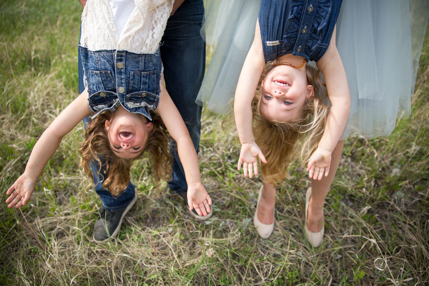 A playful family sequence of hands dangling and swinging in blue jeans against a grassy outdoor background in Canmore Alberta.